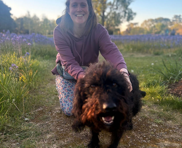 Livvy, owner of Walking Paws Around Bordon, with a large black shaggy dog in a field